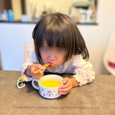モグモのコーンスープをカップからスプーンですくって食べる子ども。